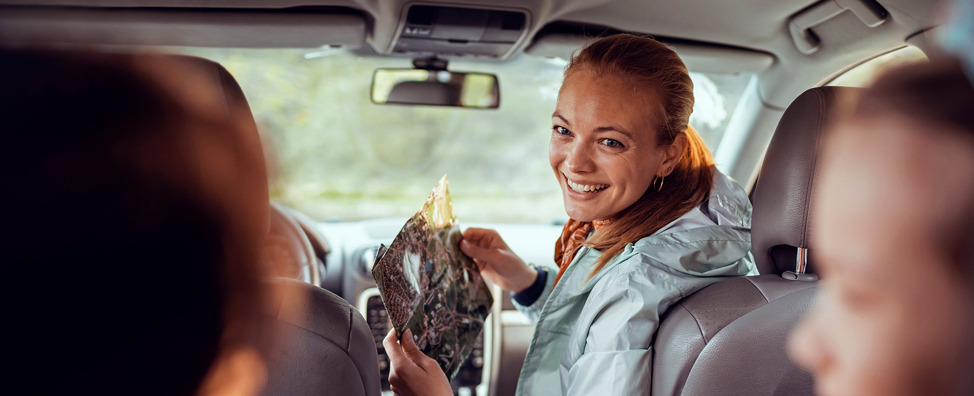 A woman holding a map and sitting in a car smiling. 